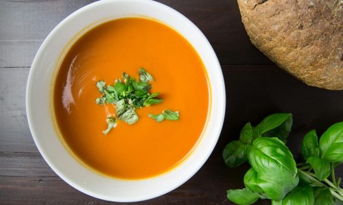 Delicious homemade tomato soup served with basil leaves and rustic bread.