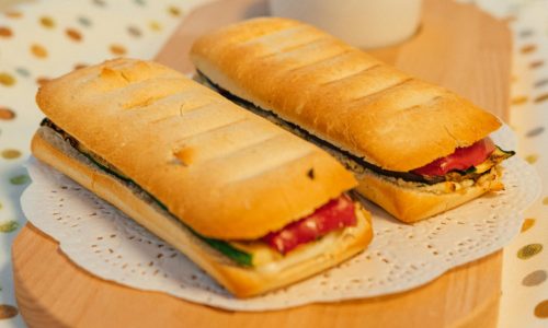 Two grilled panini sandwiches served on a wooden platter with a side of dipping sauce.