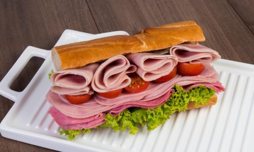 Delicious stacked ham and salami sandwich with lettuce and tomatoes on a tray.